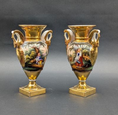 pair of gold vases with painted scenes on them sitting on a table