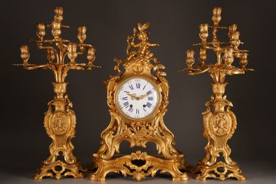 a gold clock and three candelabs on a black background