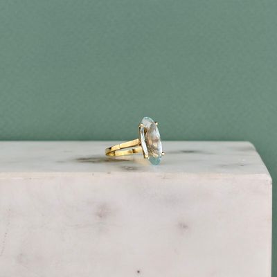 une image représentant une bague en or sertie d'une topaze bleue, posée sur un bloc de marbre