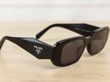 black prada sunglasses on wooden table with white wall in background