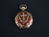 a close up of a red and gold pocket watch on a black surface