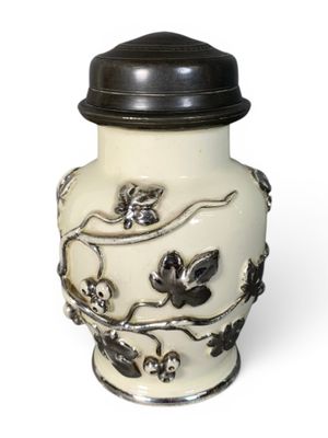un vase blanc avec un couvercle noir posé sur une surface blanche