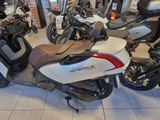 Plusieurs motos sont garées dans un showroom, autour desquelles se trouvent des personnes.