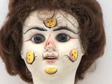 un gros plan sur le visage d'une poupée sur lequel est posé un régime de bananes
