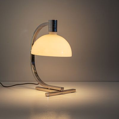 une lampe de table blanche posée sur une table, à côté d'un mur blanc