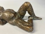 bronze statue of a woman laying on her stomach on a white surface