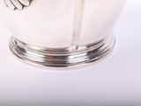 a silver vase with a bird on it on a white surface
