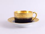 une tasse à café et une soucoupe dorées et noires posées sur une surface blanche
