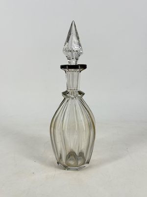 flacon de parfum en verre transparent à bouchon pointu, posé sur une surface blanche