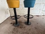 une paire de tabourets jaunes et bleus posés devant un mur de briques blanches