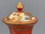 a red vase with a gold lid sitting on a table