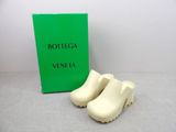 une paire de sabots blancs posée à côté d'une boîte verte de Bottega Veneta