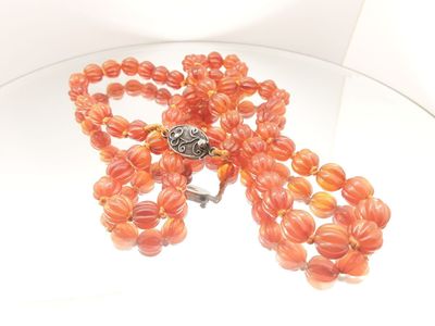 necklace with orange beads and a silver clasp on a glass table