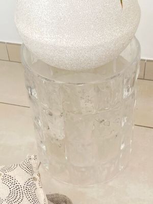 un vase en verre muni d'un couvercle, posé par terre à côté d'un petit sac