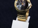 une montre en or avec un cadran noir posée sur un socle blanc