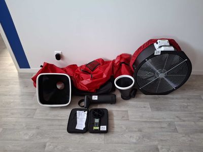 une veste rouge et un sac rouge posés par terre à côté d'un ventilateur