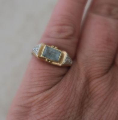 a man ' s hand holding a ring with a green stone on it