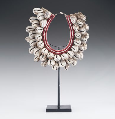 a necklace made of shells with red beads on a stand