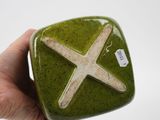 a hand holding a green ceramic object with a white cross on it