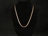 a gold necklace on a mannequin stand against a black background
