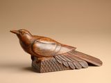 carved wooden bird sitting on top of a piece of wood