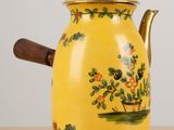 a yellow tea pot with a wooden handle on a table
