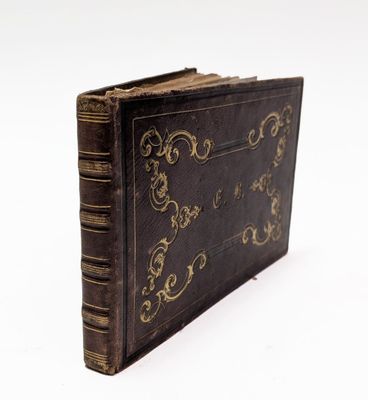 un vieux livre orné d'un motif doré, posé sur une surface blanche