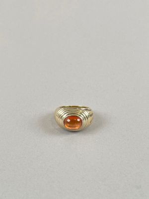 une bague en or sertie d'une pierre orange repose sur une surface blanche