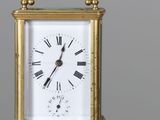 une petite horloge en or posée sur une table, avec un stylo devant