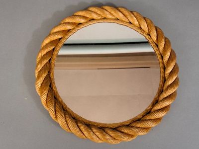 a round mirror hanging on the wall with a rope around it
