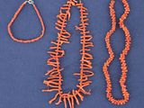 three pieces of coral necklaces and a bracelet on a blue surface