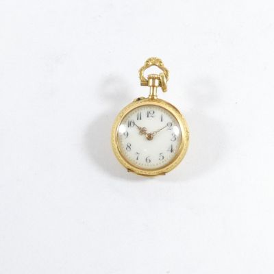 une petite montre de poche en or posée sur une surface blanche