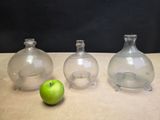 three glass vases sitting next to a green apple on a table
