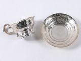 a close up of a silver cup and saucer on a white surface
