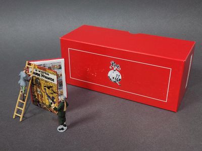 un bonhomme en jouet debout sur une échelle, à côté d'une boîte rouge sur laquelle est représenté un pompier