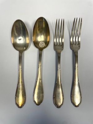 four silver spoons and a fork are lined up on a white surface