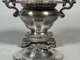 a silver vase on a silver plate with a handle