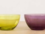purple and green glass bowls sitting on a table next to each other