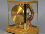 a gold clock in a glass case on a gray surface