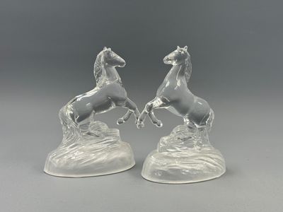 paire de figurines de chevaux en verre transparent posées sur un rocher