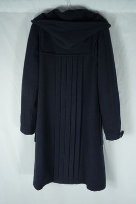 un manteau noir à capuche et à plis, accroché à un mur blanc