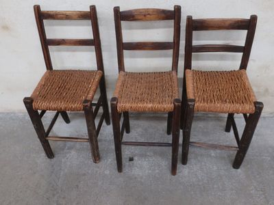 three wooden chairs with woven seats against a white wall