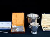 une tasse en argent, une cuillère et d'autres couverts en argent posés sur une table