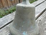 a metal bell sitting on a wooden bench in the yard