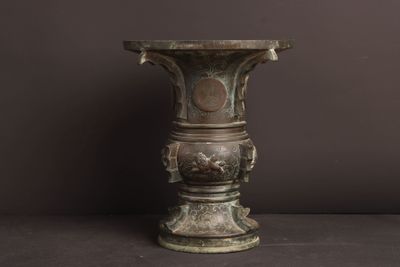 un vase antique en bronze posé sur une table, sur un fond sombre