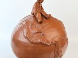 une sculpture en argile représentant un homme assis sur une pomme