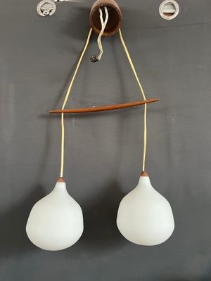 deux lampes en verre blanc suspendues à un poteau en bois sur un mur gris