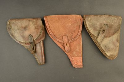 three leather holsters are lined up on a gray surface