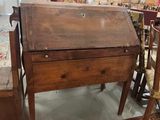 un bureau et une chaise en bois dans une pièce où sont accrochés des tableaux au mur