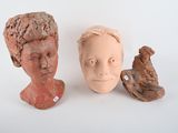 two clay heads of people and a bird on a white surface